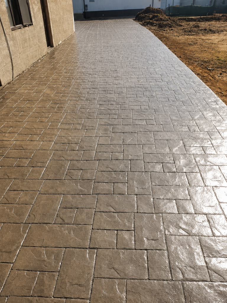 Entrada de vivienda con hormigón impreso efecto adoquín en tonos gris y antracita, con acabado brillante y alta resistencia para exteriores.